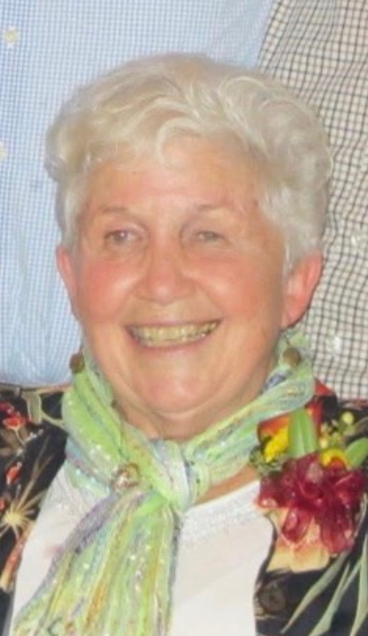 A smiling portrait of Betty Walsh wearing a green scarf and a red flower